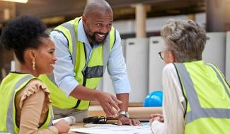 man in safety vest going over plans with 2 women