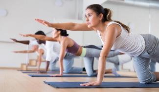 woman and men yoga class on floor on knee reaching one arm forward